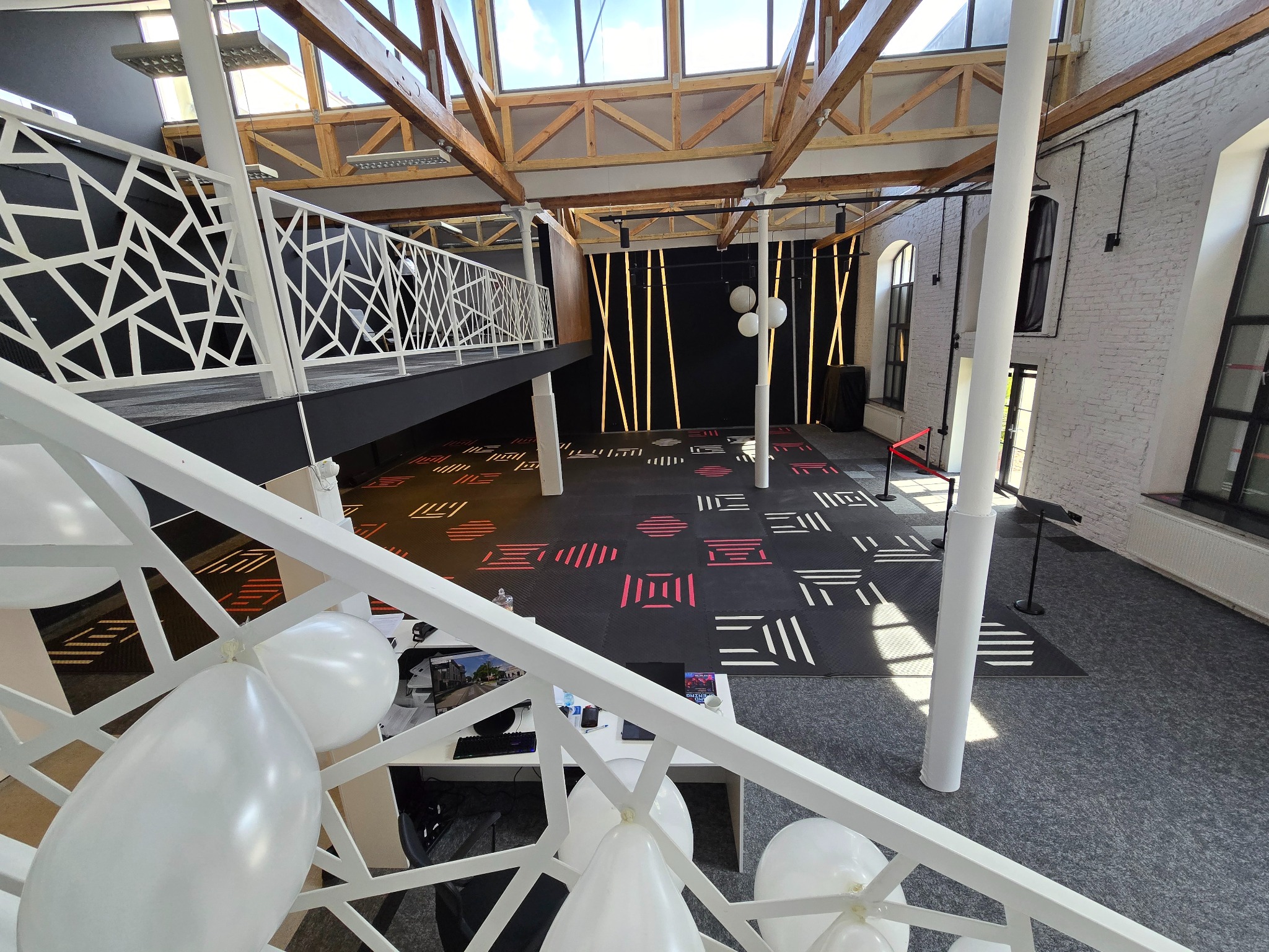 Przestronne, nowoczesne wnętrze sali z antresolą, dekoracjami świetlnymi i białymi balonami, przygotowane na wydarzenie.