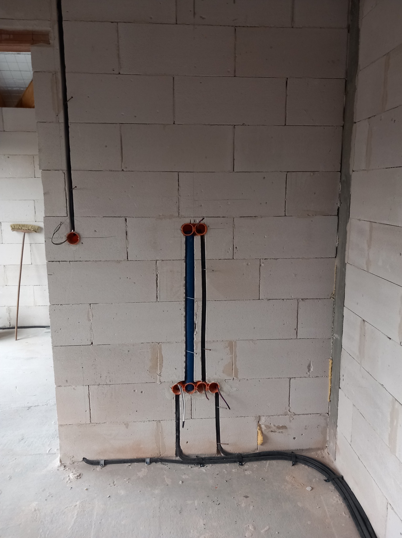 Instalacja elektryczna w ścianie z betonu komórkowego: kable w peszlach, puszki instalacyjne. Widoczne przewody i mocowania. Surowy stan, przygotowanie do tynkowania.