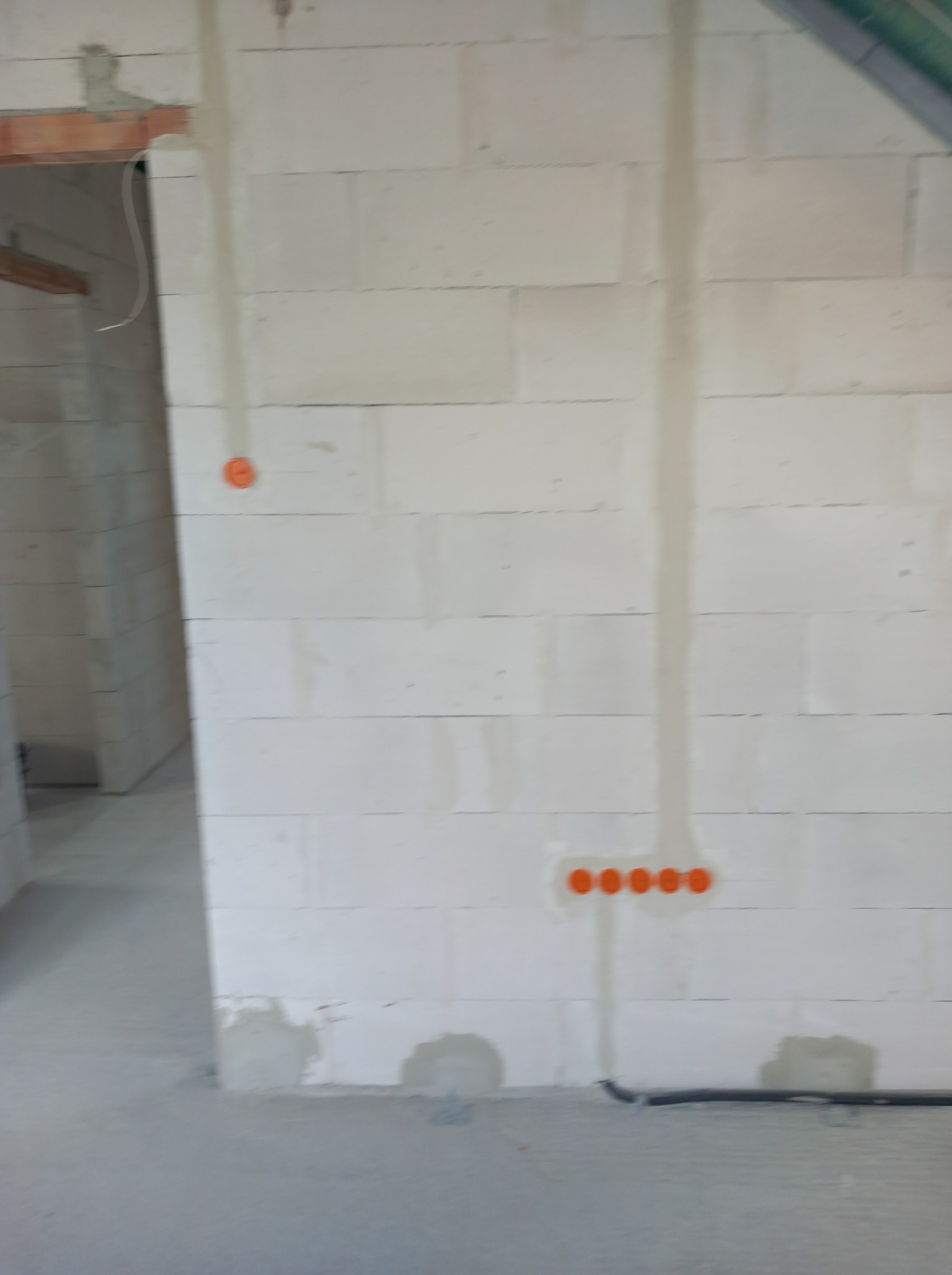 Ściana z betonu komórkowego z widocznymi puszkami instalacyjnymi w kolorze pomarańczowym i przewodami. Surowy stan wykończenia wnętrza.