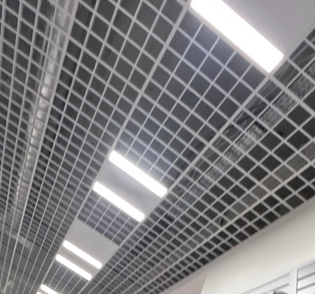 Metalowa siatka sufitowa z wbudowanymi, podłużnymi lampami LED, widok z dołu pod kątem.