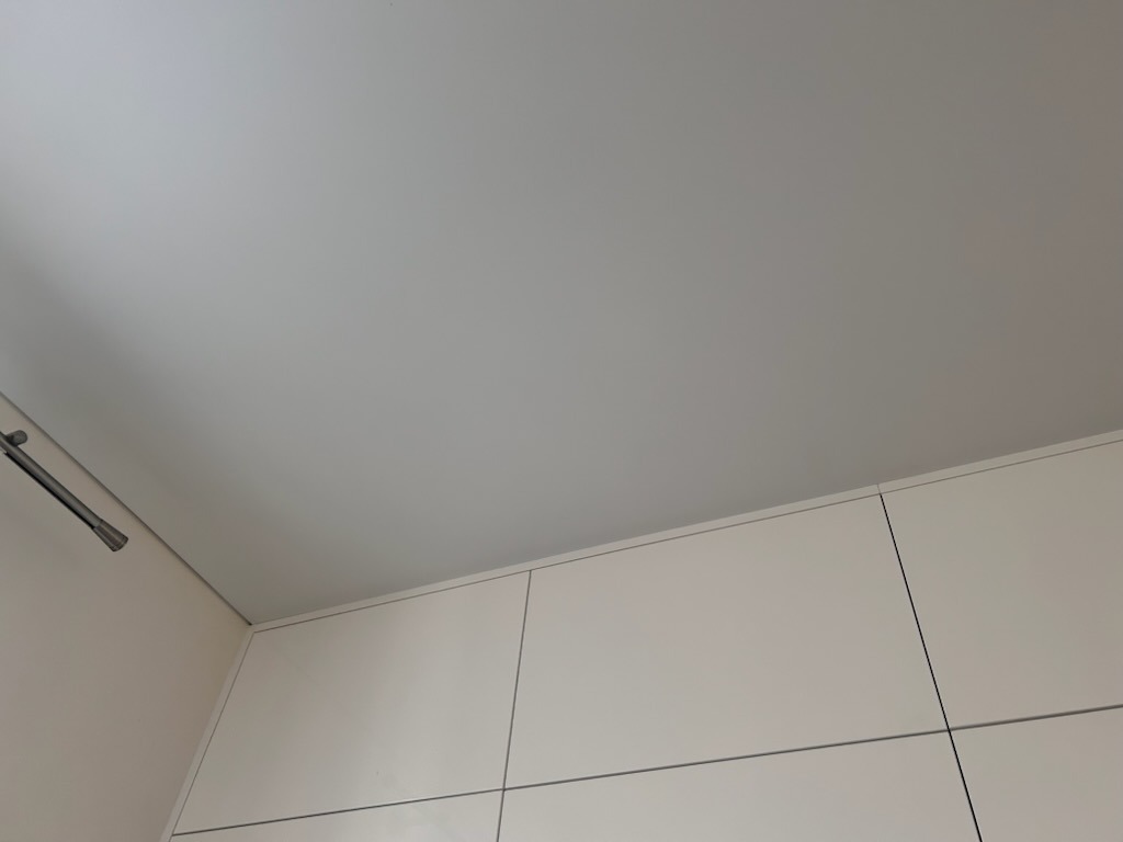 Jasnoszary sufit napinany z widoczną szyną oświetleniową i górną częścią białych szafek kuchennych.