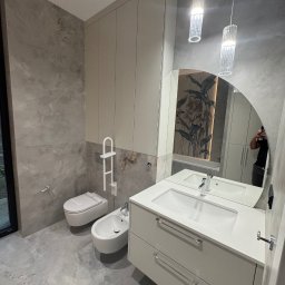 OK-Bud Oleh Kopytko - Nowoczesna łazienka w szarościach z marmurowymi płytkami, podwieszana toaleta i bidet, szafka z umywalką z dwoma szufladami oraz wysoka szafka zabudowana od podłogi do sufitu, oświetlenie w postaci...