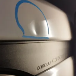 Wgniecenie na białym błotniku samochodu Toyota Corolla Cross, zaznaczone niebieską obwódką przed naprawą.