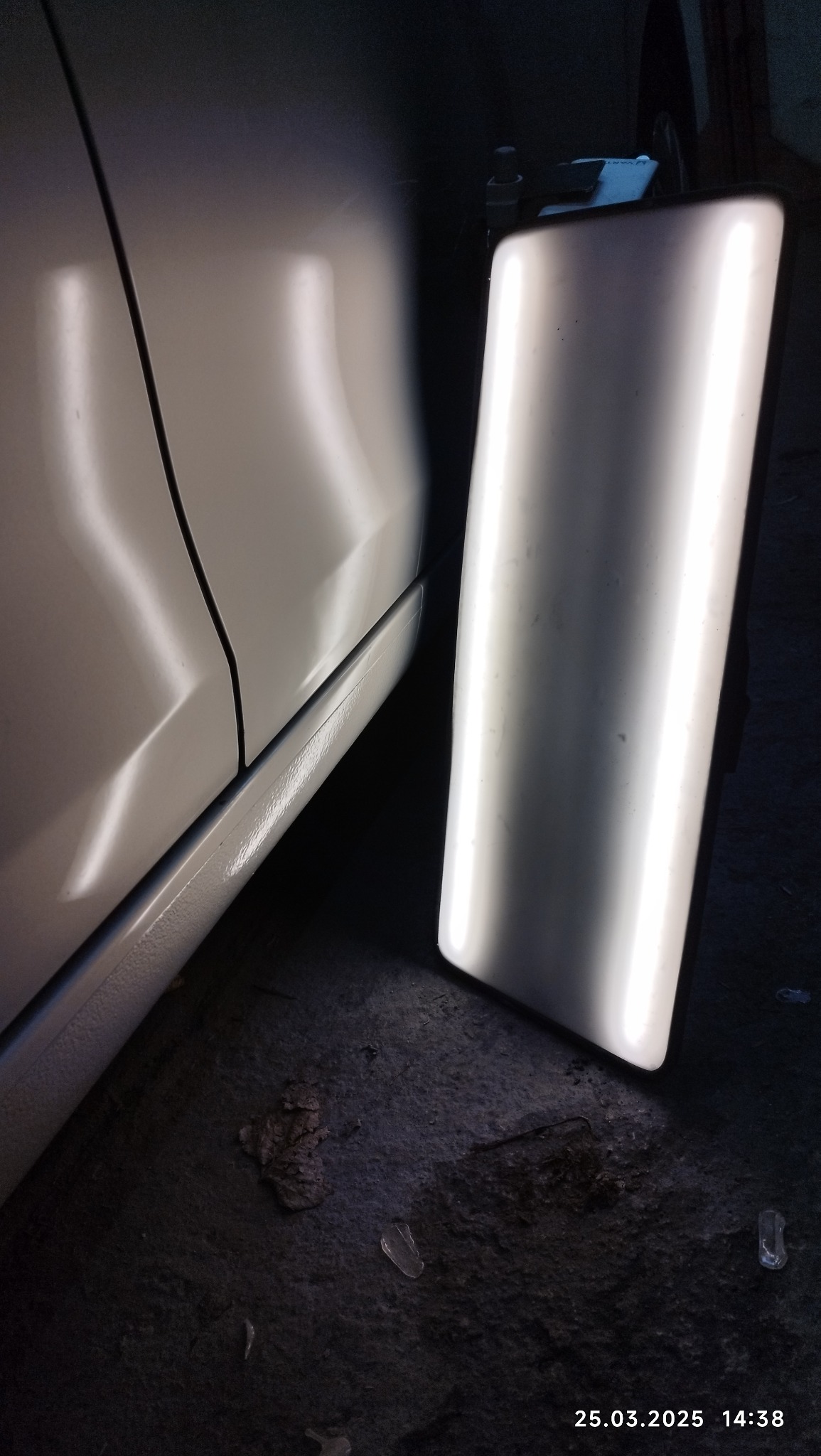 Błonie: Reflektor warsztatowy oświetla bok białego samochodu podczas naprawy karoserii. Widoczny fragment progu i drzwi auta.