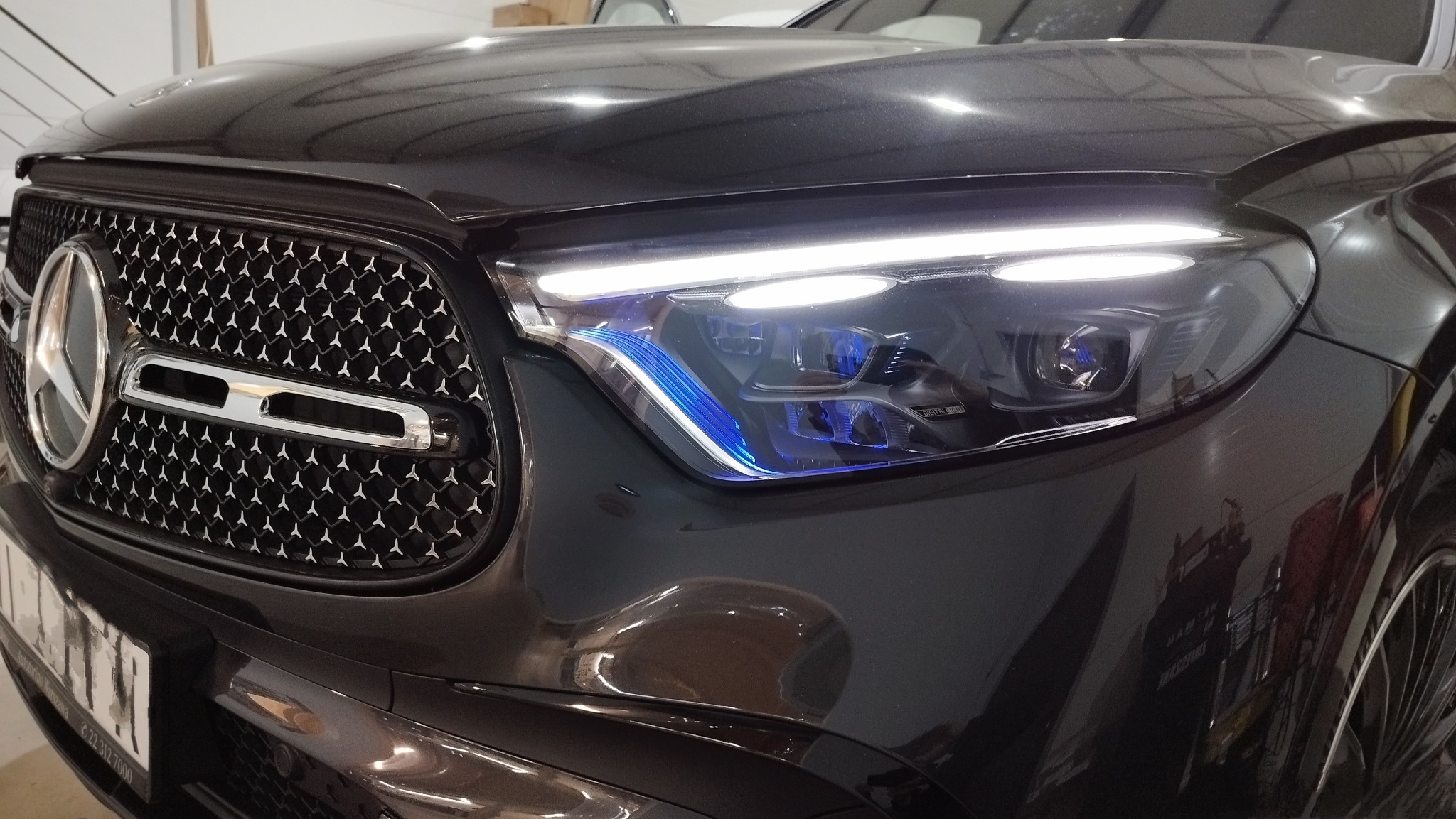 Czarny samochód marki Mercedes z chromowaną atrapą chłodnicy i reflektorami z niebieską poświatą.