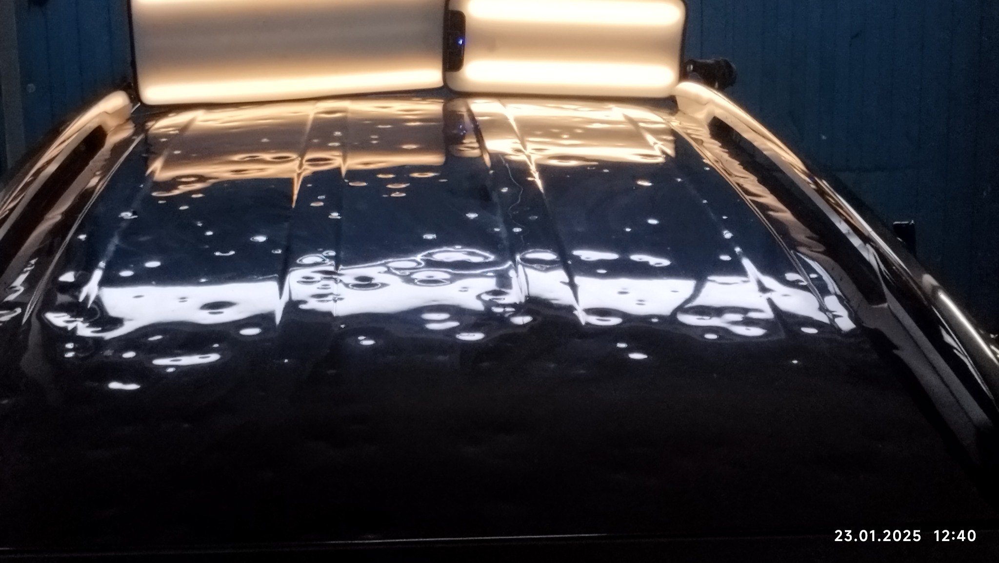 Błyszczący dach samochodu z widocznymi wgnieceniami podświetlony lampami warsztatowymi, przygotowany do naprawy karoserii.