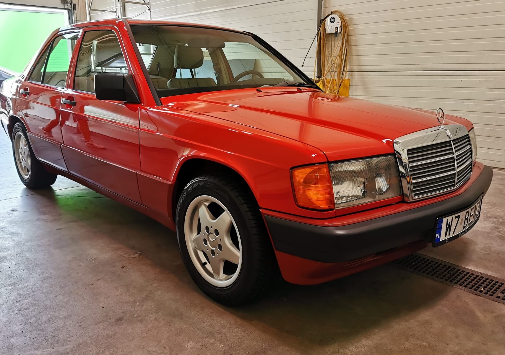 Czerwony Mercedes-Benz W201 po renowacji lakieru, widoczny chromowany grill i felgi z gwiazdą, zaparkowany w garażu.