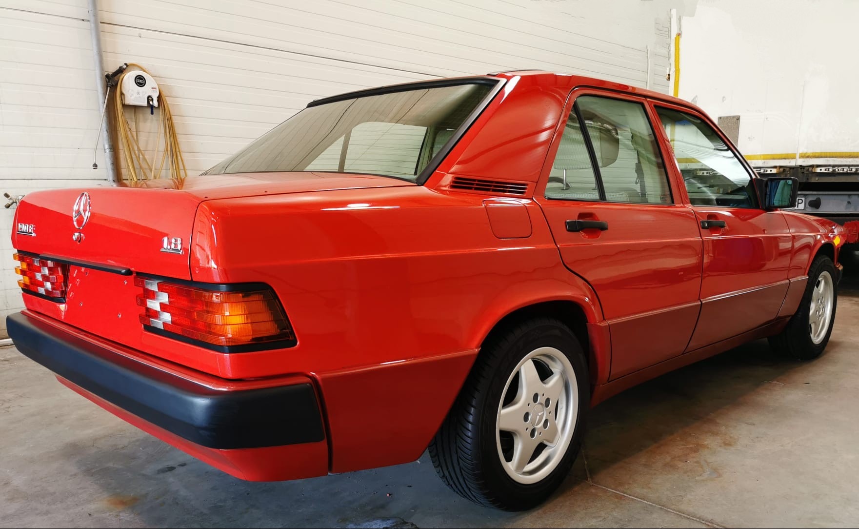 Czerwony Mercedes-Benz 190E 1.8 po renowacji lakieru, widok z tyłu, charakterystyczne kanciaste nadwozie i aluminiowe felgi w kształcie gwiazdy.