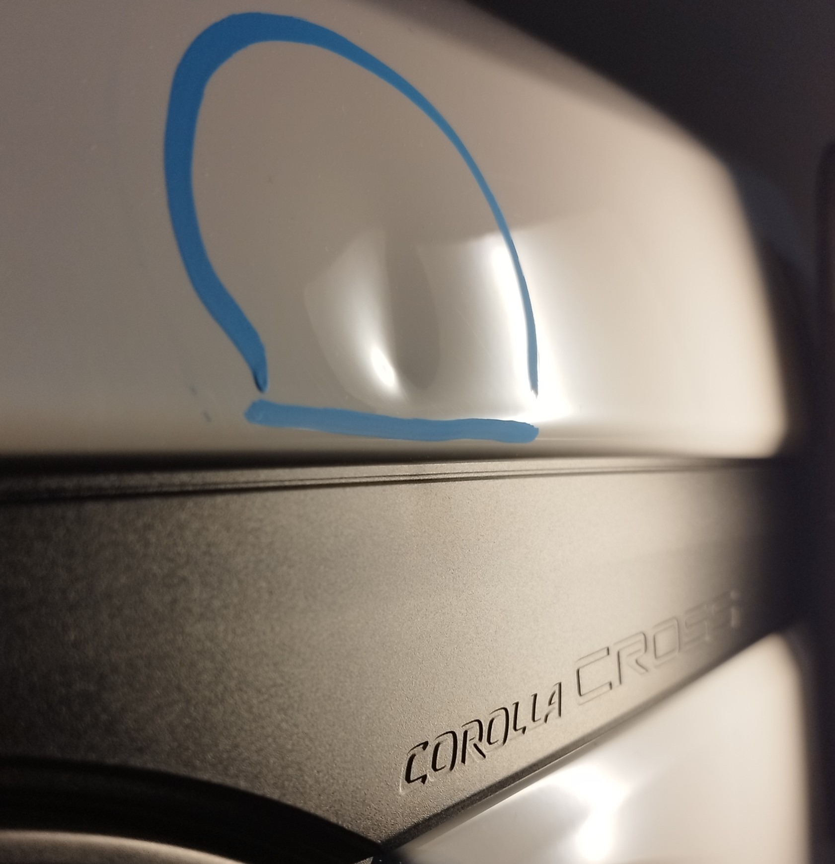 Wgniecenie na białym błotniku samochodu Toyota Corolla Cross, zaznaczone niebieską obwódką przed naprawą.