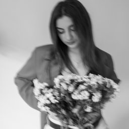 Patrycja Niedzielska - Czarno-białe zdjęcie kobiety z bukietem kwiatów, ubrana w marynarkę i dżinsy. Patrzy w dół na kwiaty, z delikatnym uśmiechem. Rozmycie dodaje dynamiki.
