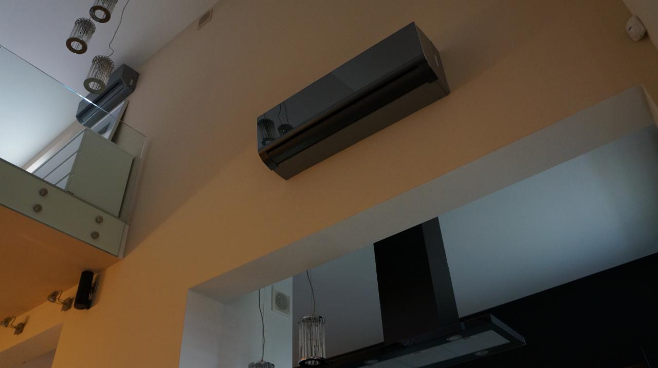 Elegancki, czarny klimatyzator ścienny w nowoczesnym wnętrzu z widocznym fragmentem antresoli i oświetleniem. Nietypowy kąt ujęcia.