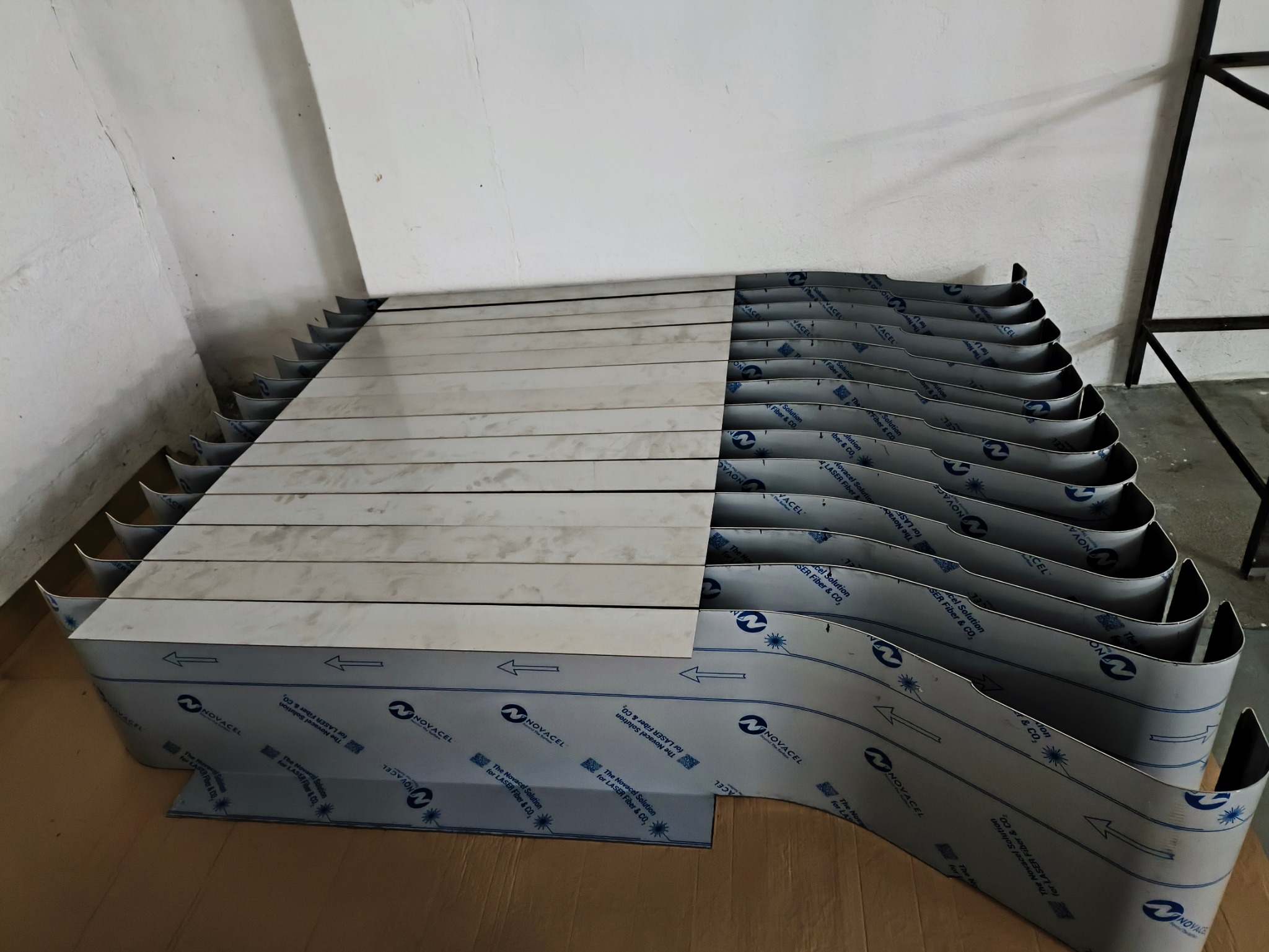 Stos arkuszy blachy nierdzewnej z folią ochronną Novacel, przygotowanych do dalszej obróbki w Ełku, ułożonych warstwami na tekturze.