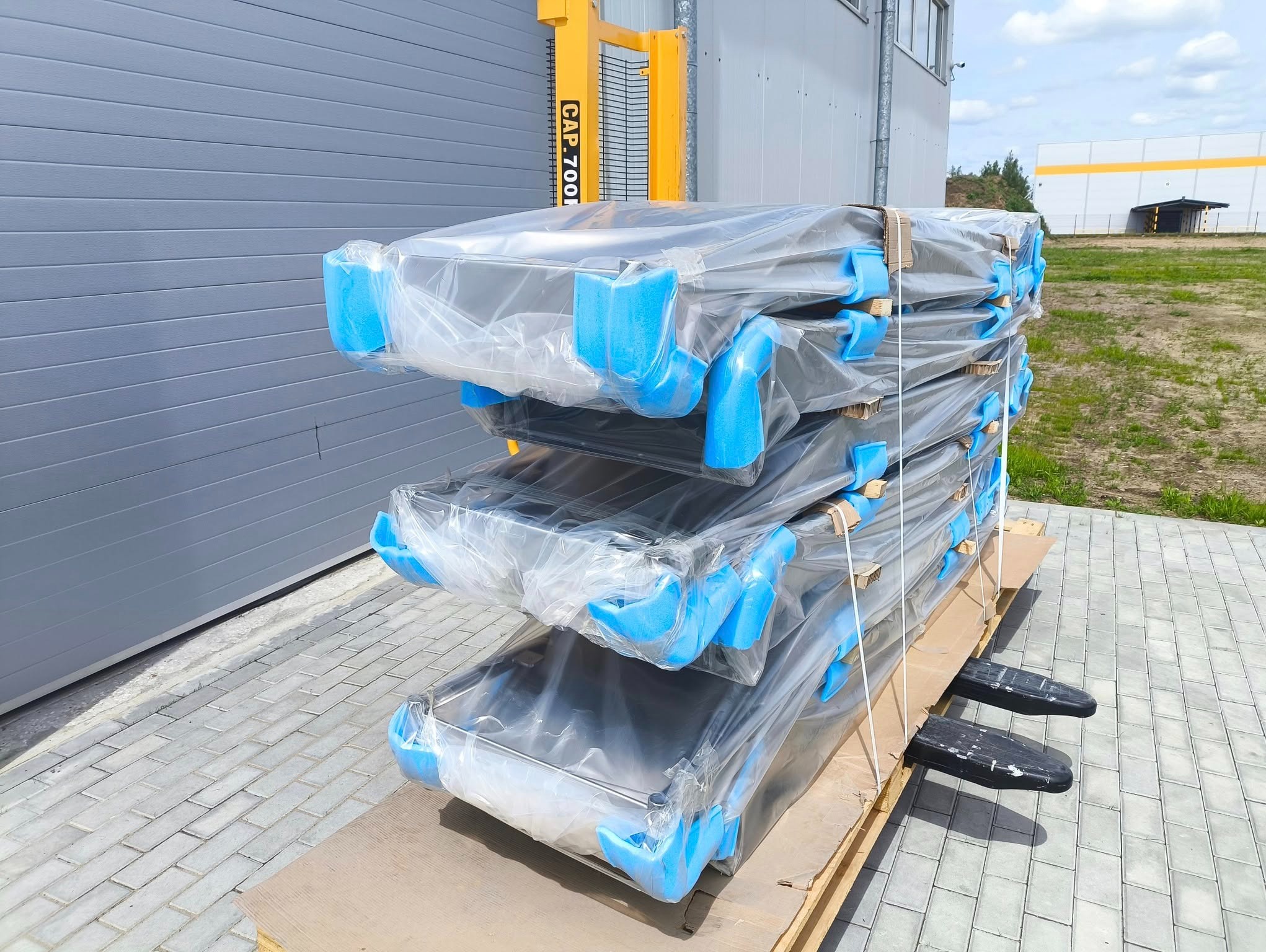 Stos zabezpieczonych, metalowych wanien o srebrnej barwie, owiniętych folią i zabezpieczonych niebieską pianką, ułożonych na palecie, gotowych do transportu.