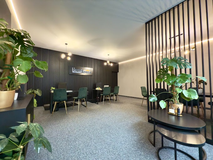 Nowoczesne biuro agencji nieruchomości z czarnymi ścianami z lameli, zielonymi krzesłami i roślinami doniczkowymi, oświetlone kulistymi lampami.