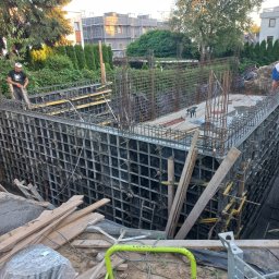 VegasBUD - Wykop pod fundamenty z szalunkiem systemowym i zbrojeniem, widoczny pracownik w tle oraz zagęszczarka wibracyjna na pierwszym planie.