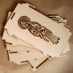 Stos drewnianych, wyciętych laserowo elementów z motywem stylizowanej postaci anioła, przygotowanych do złożenia w pudełko lub ozdobę.
