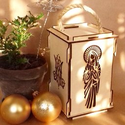 PRUS CAPITAL SPÓŁKA Z OGRANICZONĄ ODPOWIEDZIALNOŚCIĄ - Ozdobna, drewniana lampionowa skrzynka z wyciętym laserowo motywem religijnym, stojąca obok doniczki z ostrokrzewem i złotymi bombkami. Produkt dostępny w Toruniu.