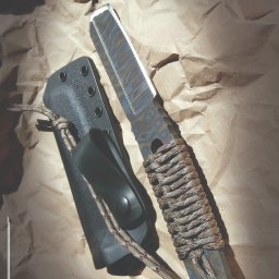 PRUS CAPITAL SPÓŁKA Z OGRANICZONĄ ODPOWIEDZIALNOŚCIĄ - Nóż o surowym wykończeniu, z rękojeścią owiniętą sznurkiem, leżący obok czarnej pochwy na tle zmiętego papieru.