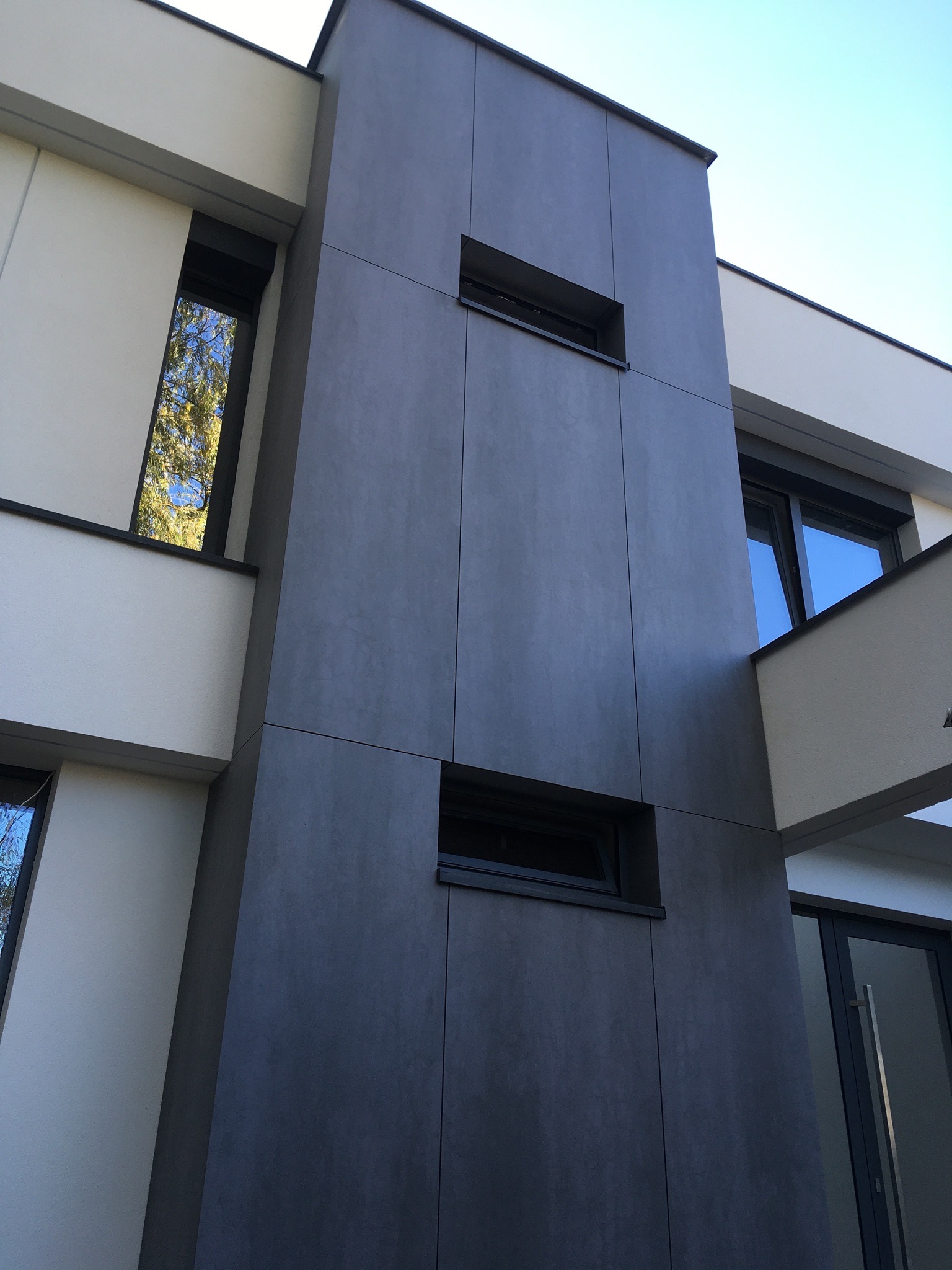 Nowoczesna elewacja budynku z szarymi panelami i małymi, prostokątnymi oknami, widok z dołu.