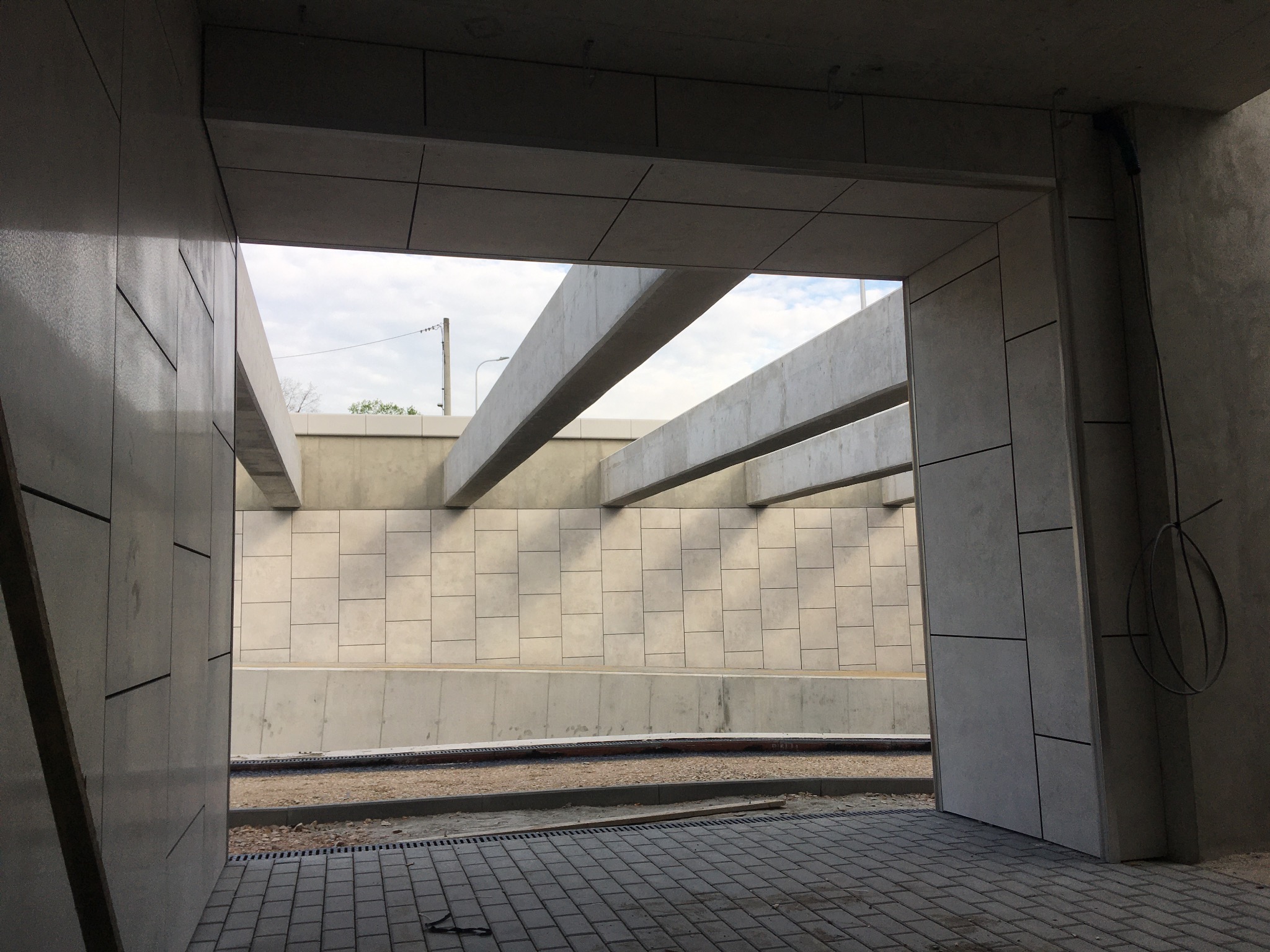 Nowoczesna elewacja z płyt w odcieniach szarości, widok z wnętrza budynku. Minimalistyczny design z geometrycznym układem płyt i betonowymi elementami konstrukcyjnymi.