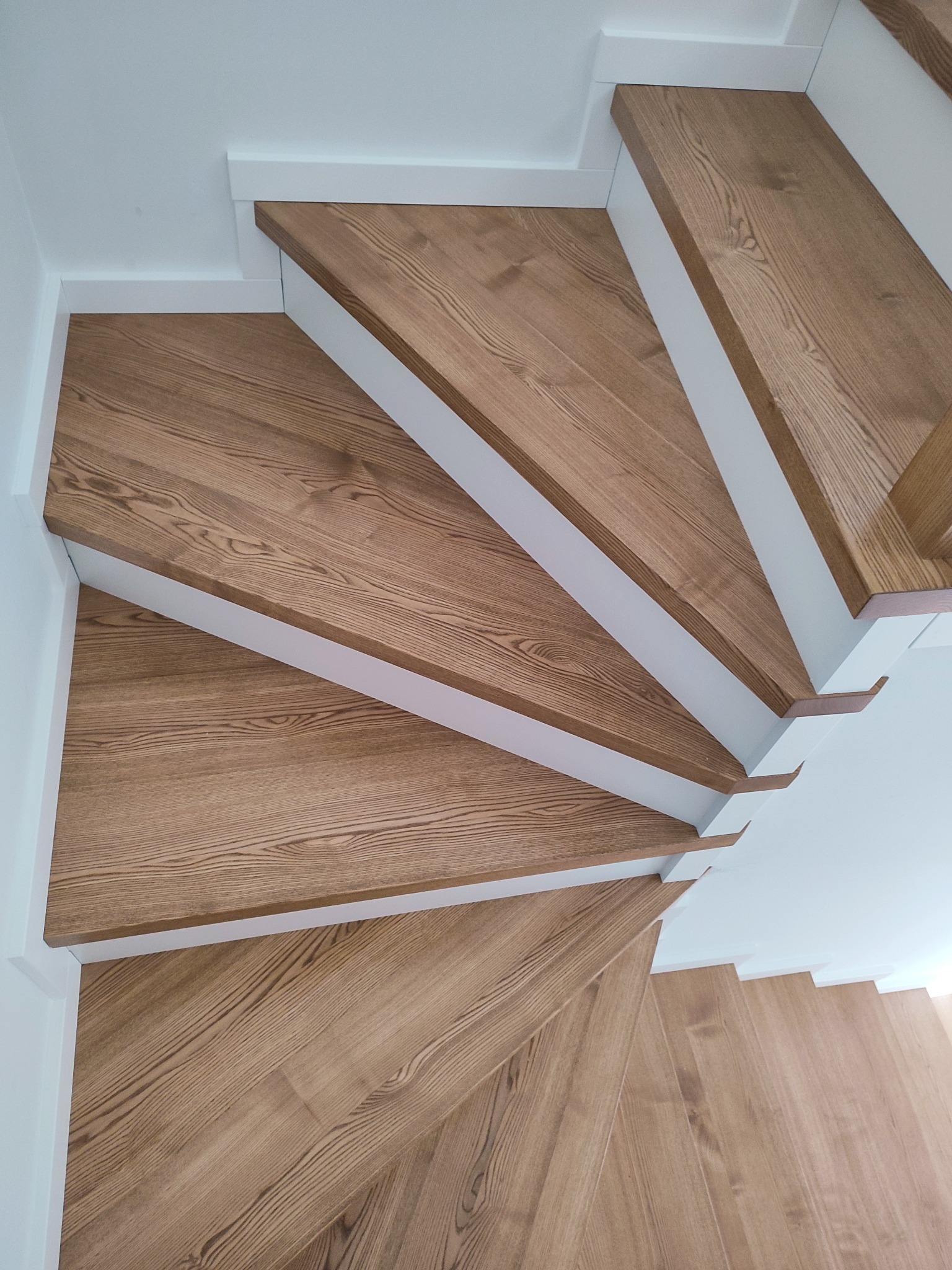 Wewnętrzne schody z drewnianymi stopniami o jasnym odcieniu dębu, z białymi podstopnicami i listwami przypodłogowymi.