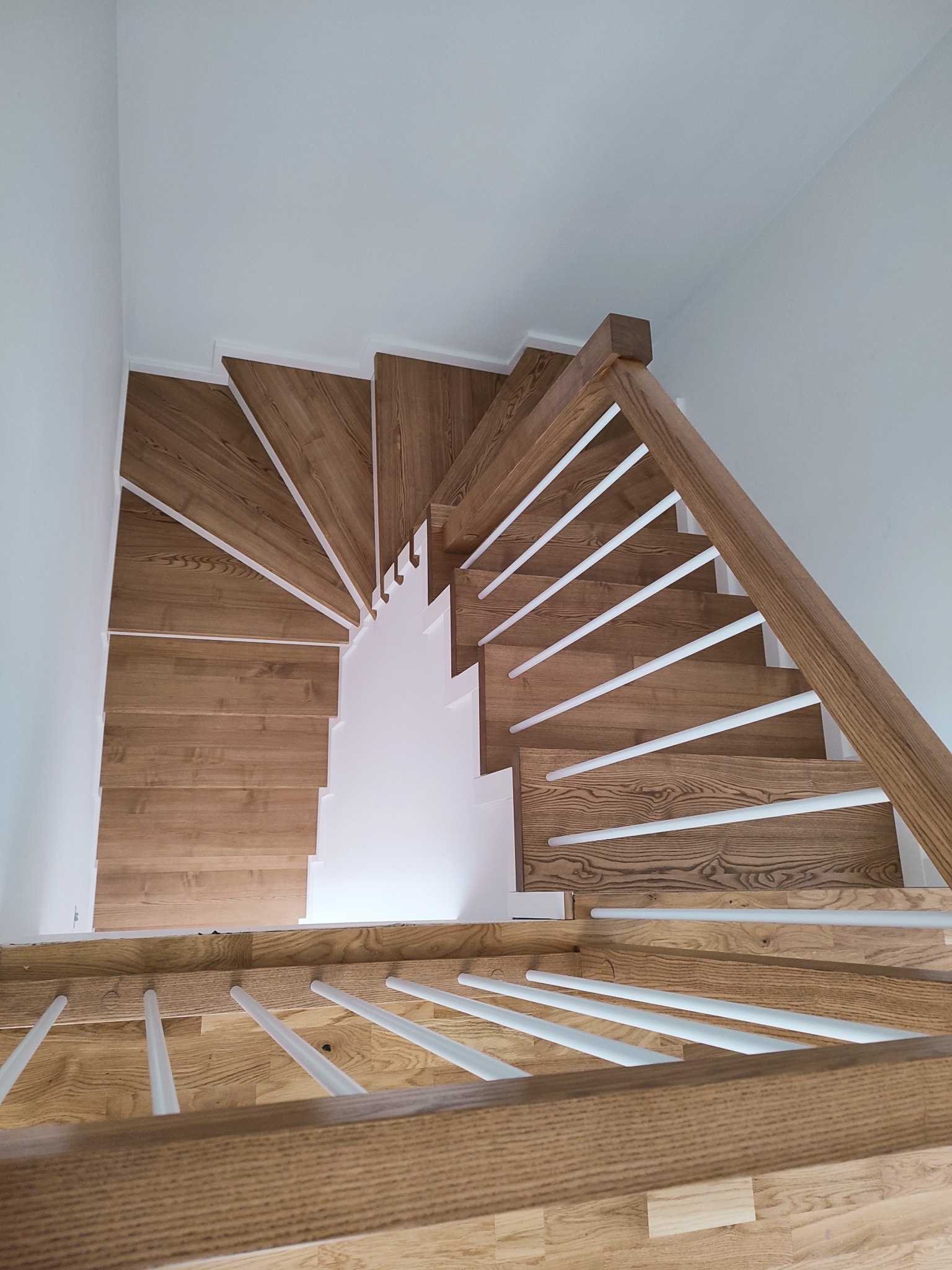 Widok z góry na kręte schody drewniane z białymi balustradami w nowoczesnym wnętrzu, jasne drewno, minimalistyczny design.