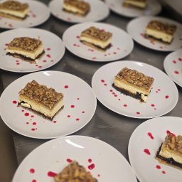 Ludowa - Porcje ciasta orzechowego na białych talerzach, udekorowane kroplami czerwonego sosu, gotowe do serwowania. Widok z góry, ostre światło.