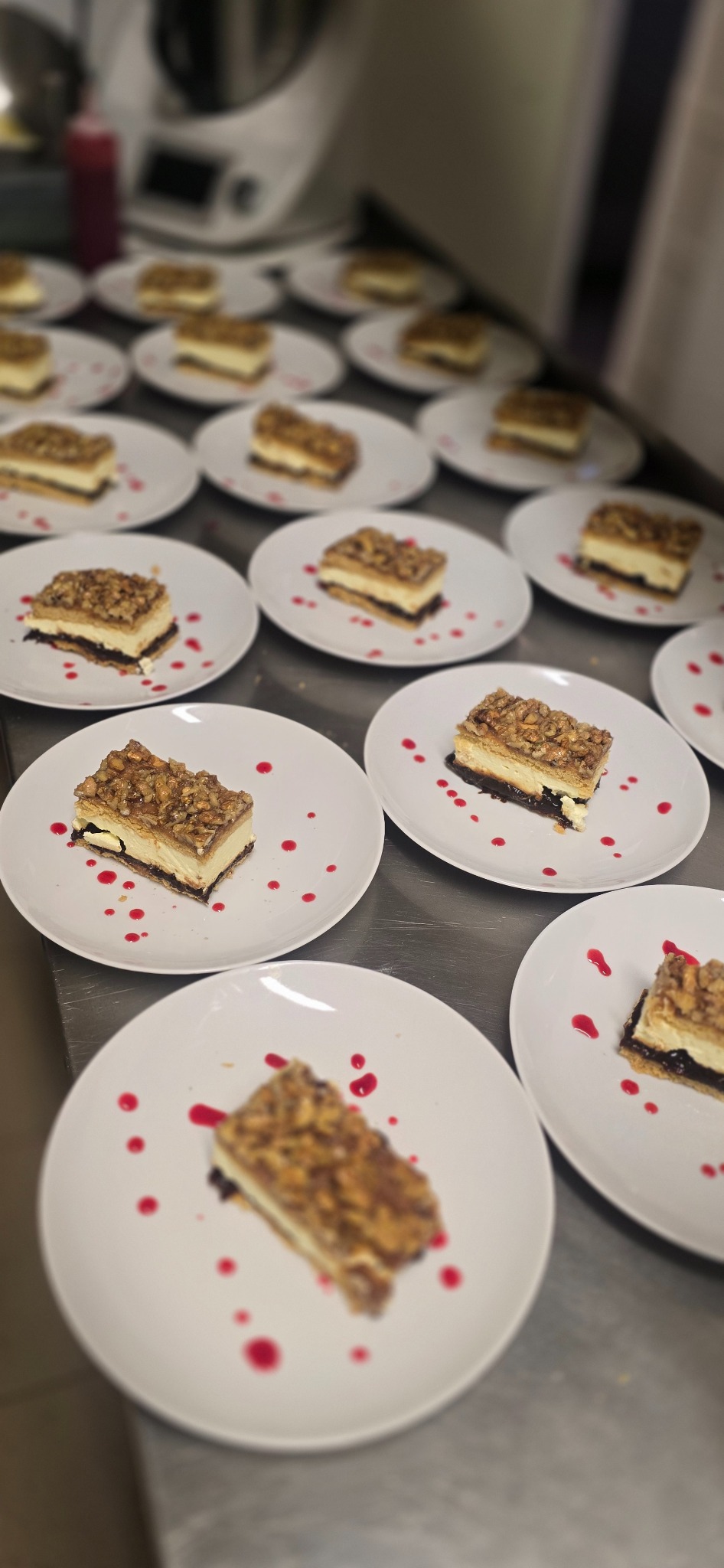 Porcje ciasta orzechowego na białych talerzach, udekorowane kroplami czerwonego sosu, gotowe do serwowania. Widok z góry, ostre światło.