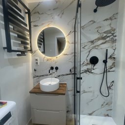 DAN-HOUSE SPÓŁKA Z OGRANICZONĄ ODPOWIEDZIALNOŚCIĄ - Nowoczesna łazienka z kabiną prysznicową typu walk-in, umywalką nablatową i okrągłym lustrem z podświetleniem LED. Marmurowe płytki na ścianach i czarne akcenty armatury.