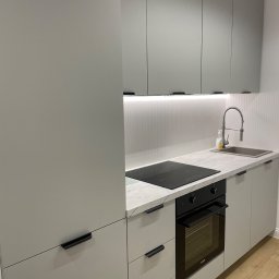 DAN-HOUSE SPÓŁKA Z OGRANICZONĄ ODPOWIEDZIALNOŚCIĄ - Nowoczesna, szara zabudowa kuchenna z marmurowym blatem, czarną płytą indukcyjną i piekarnikiem. Ujęcie z bliska, widoczne detale wykończenia i armatura.