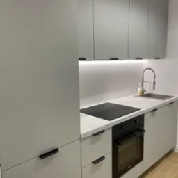 Nowoczesna, szara zabudowa kuchenna z marmurowym blatem, czarną płytą indukcyjną i piekarnikiem. Ujęcie z bliska, widoczne detale wykończenia i armatura.