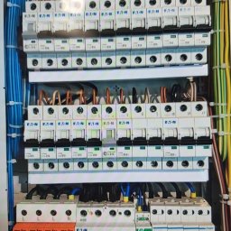 Elmack - Rozdzielnica elektryczna z zabezpieczeniami przepięciowymi, wyłącznikami nadprądowymi Eaton i okablowaniem w różnych kolorach, zainstalowana w obudowie.