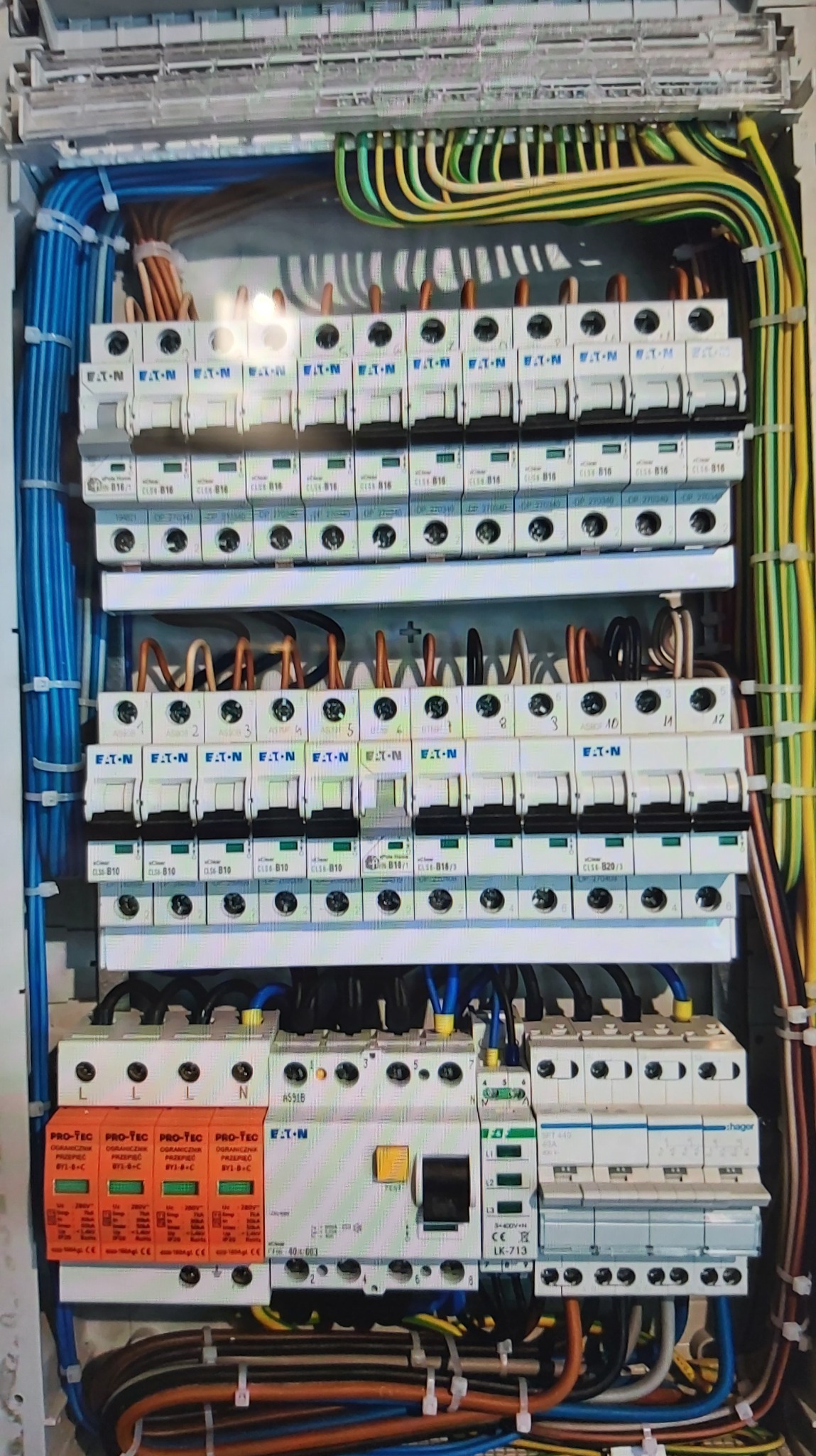 Rozdzielnica elektryczna z zabezpieczeniami przepięciowymi, wyłącznikami nadprądowymi Eaton i okablowaniem w różnych kolorach, zainstalowana w obudowie.