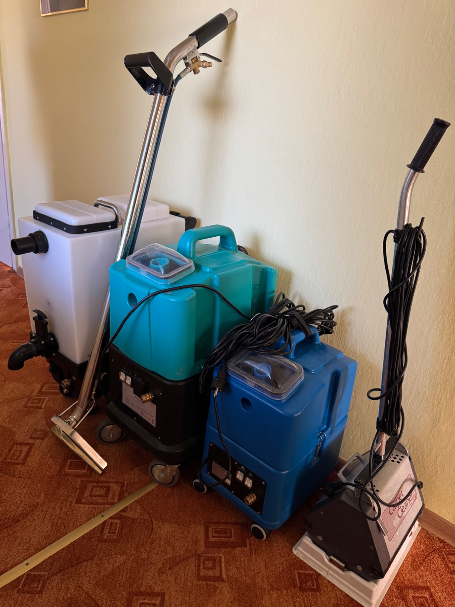 Profesjonalne urządzenia do czyszczenia tekstylnych powierzchni: biały odkurzacz piorący z lancą, turkusowy i niebieski odkurzacz z przezroczystymi pokrywami oraz kompaktowy odkurzacz do dywanów...