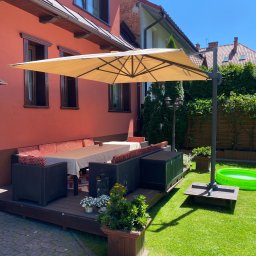 Leśnicki Stolarstwo - Zadaszony taras drewniany z meblami ogrodowymi i parasolem, obok zielony trawnik z basenem dla dzieci.