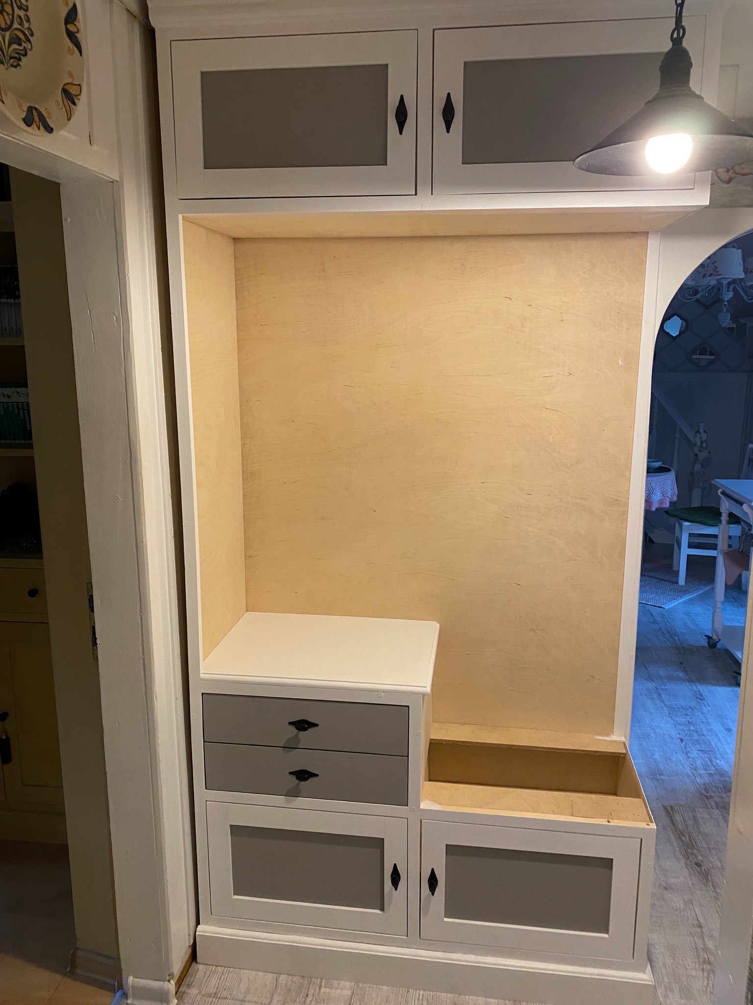 Wnęka w przedpokoju z zabudową w trakcie montażu, widoczne szare fronty szafek i szuflad z czarnymi uchwytami, oraz surowe drewniane wnętrze.