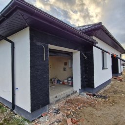 TERMIKA Paweł Józwik - Dwukondygnacyjny budynek z białą elewacją i czarnymi elementami dekoracyjnymi, w trakcie prac wykończeniowych. Widoczne materiały budowlane i pracownicy.