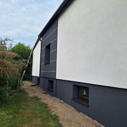TERMIKA Paweł Józwik - Dwukolorowa elewacja domu z oknami piwnicznymi i drabiną opartą o ścianę. Biała góra i grafitowy dół z pasami. Świeżo wykonana elewacja.