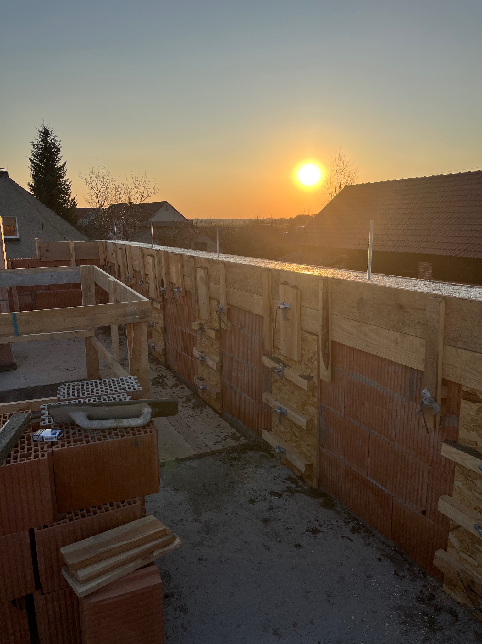 Wznoszenie ścian domu z pustaków ceramicznych, szalunki drewniane, widok na zachodzące słońce.