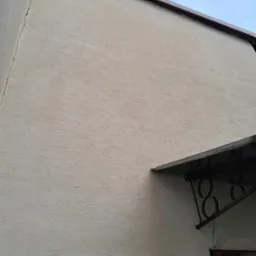 Jasna elewacja budynku z widocznym zadaszeniem nad wejściem i numerem domu wykonanym z metalu.