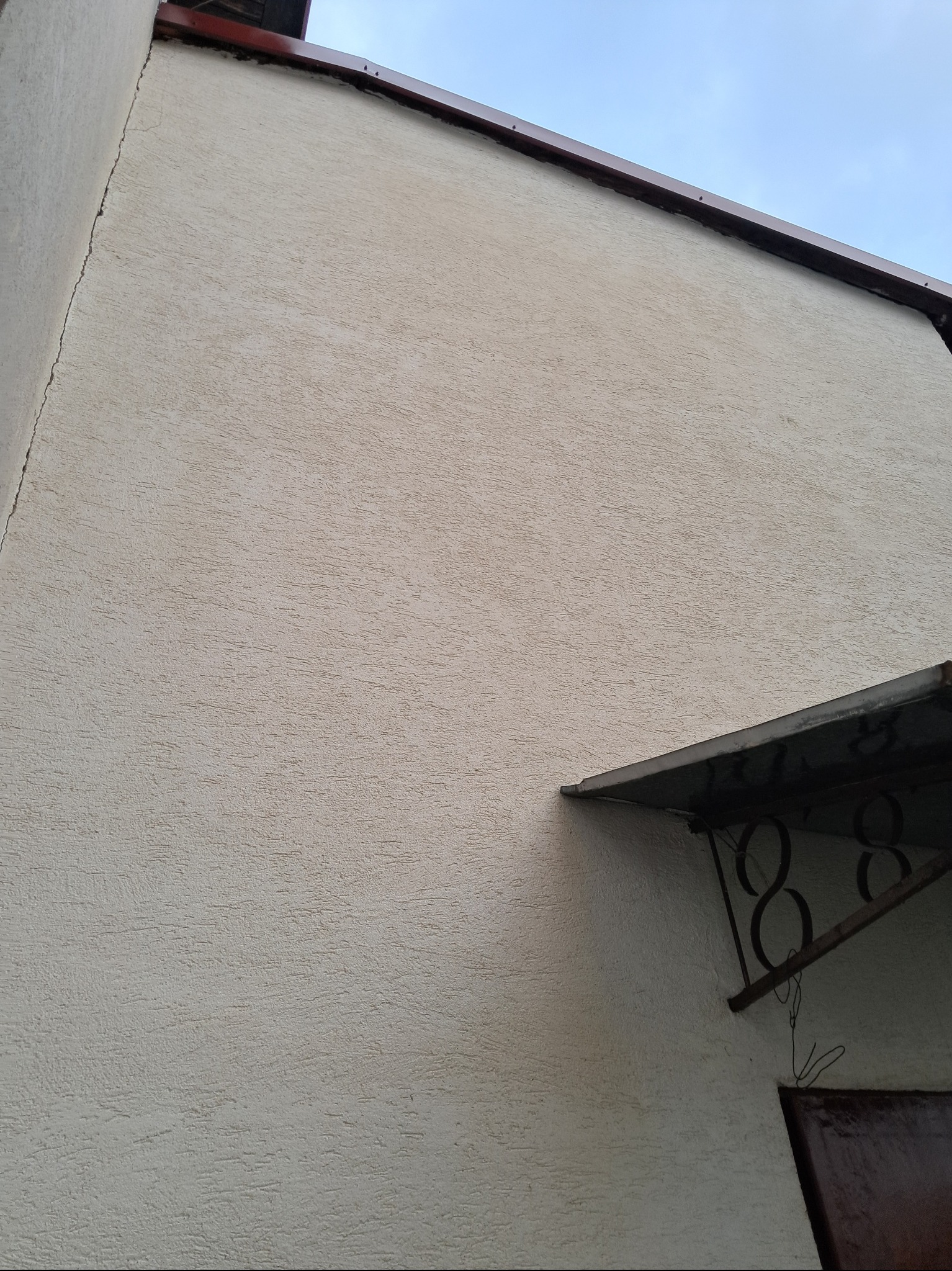 Jasna elewacja budynku z widocznym zadaszeniem nad wejściem i numerem domu wykonanym z metalu.