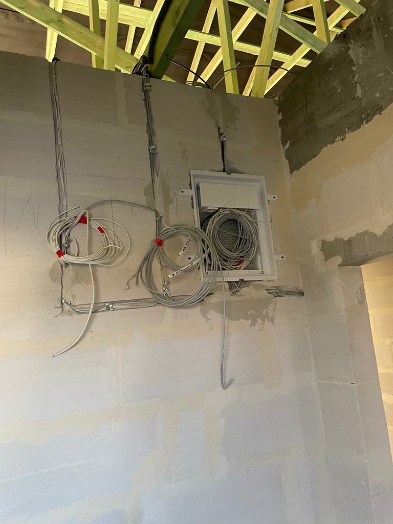 Wewnętrzna instalacja elektryczna w surowym stanie: przewody prowadzone po ścianach, puszka rozdzielcza z nawiniętymi kablami, drewniana konstrukcja dachu.