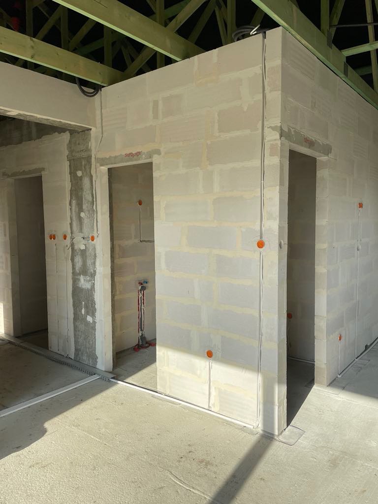 Wewnętrzne ściany z betonu komórkowego w stanie surowym w Łubiance, z widocznymi przewodami elektrycznymi w peszlach, przygotowane do dalszych prac wykończeniowych.