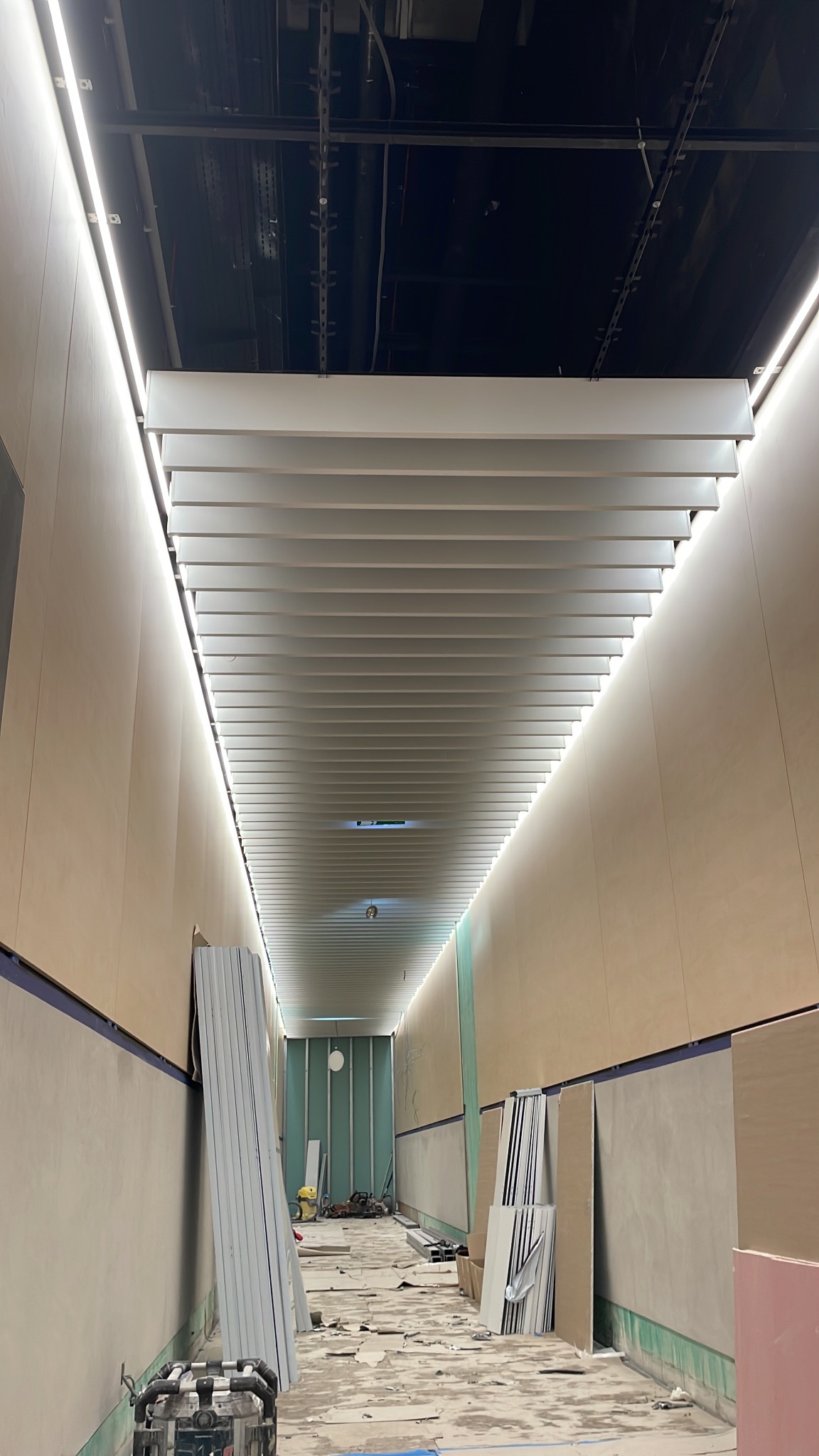 Korytarz w trakcie remontu z zamontowanym, nowoczesnym oświetleniem LED pod sufitem z białych lameli.
