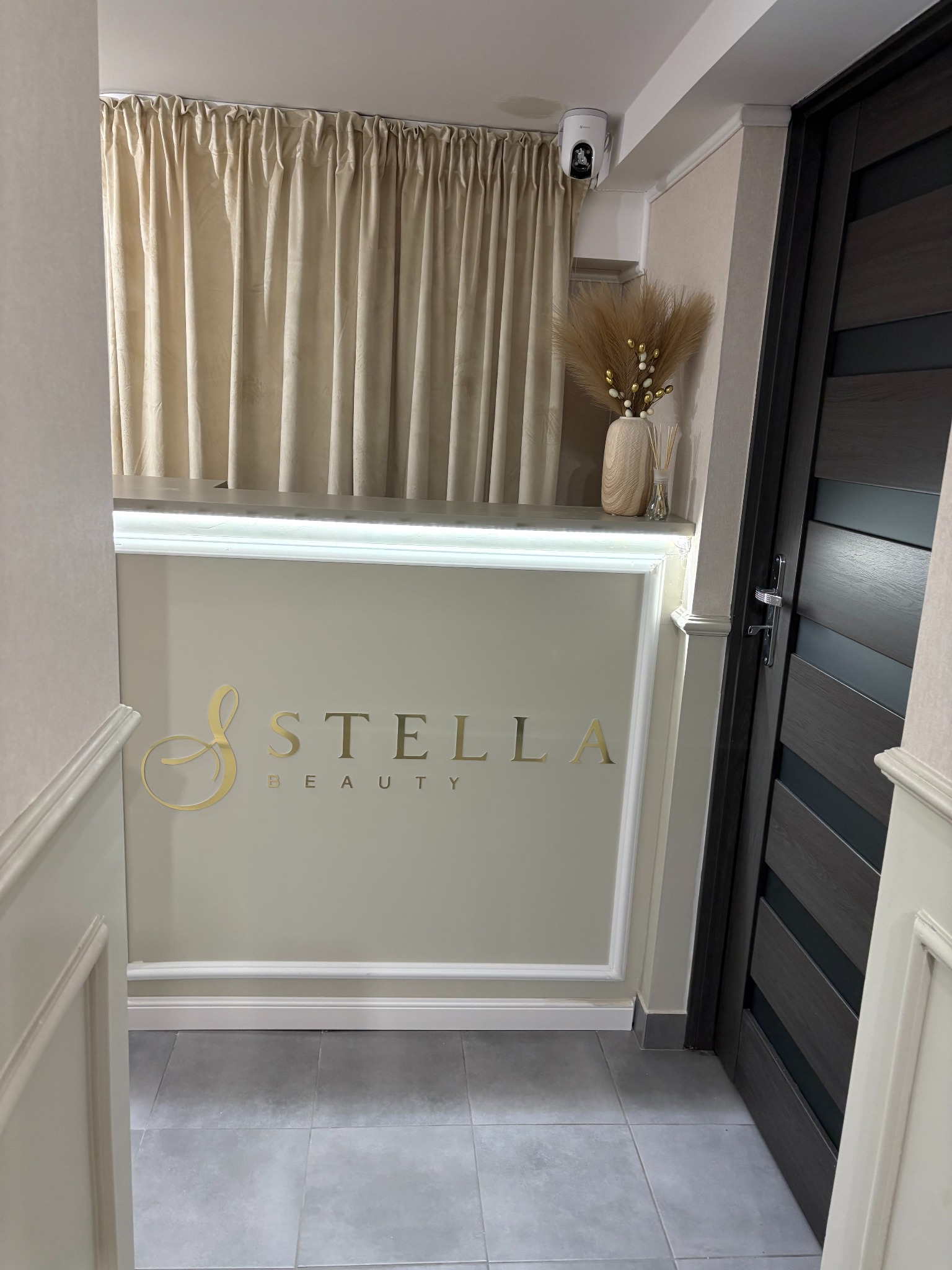 Recepcja z podświetlanym blatem w salonie kosmetycznym Stella Beauty, z dekoracyjnymi zasłonami i wazonem z suszonymi trawami.