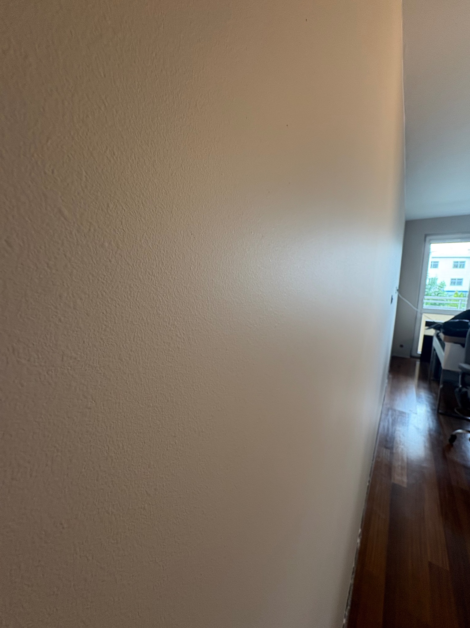 Ściana w odcieniach beżu po malowaniu, widoczna faktura, z parkietem i oknem w tle. Minimalistyczne wnętrze po odświeżeniu.