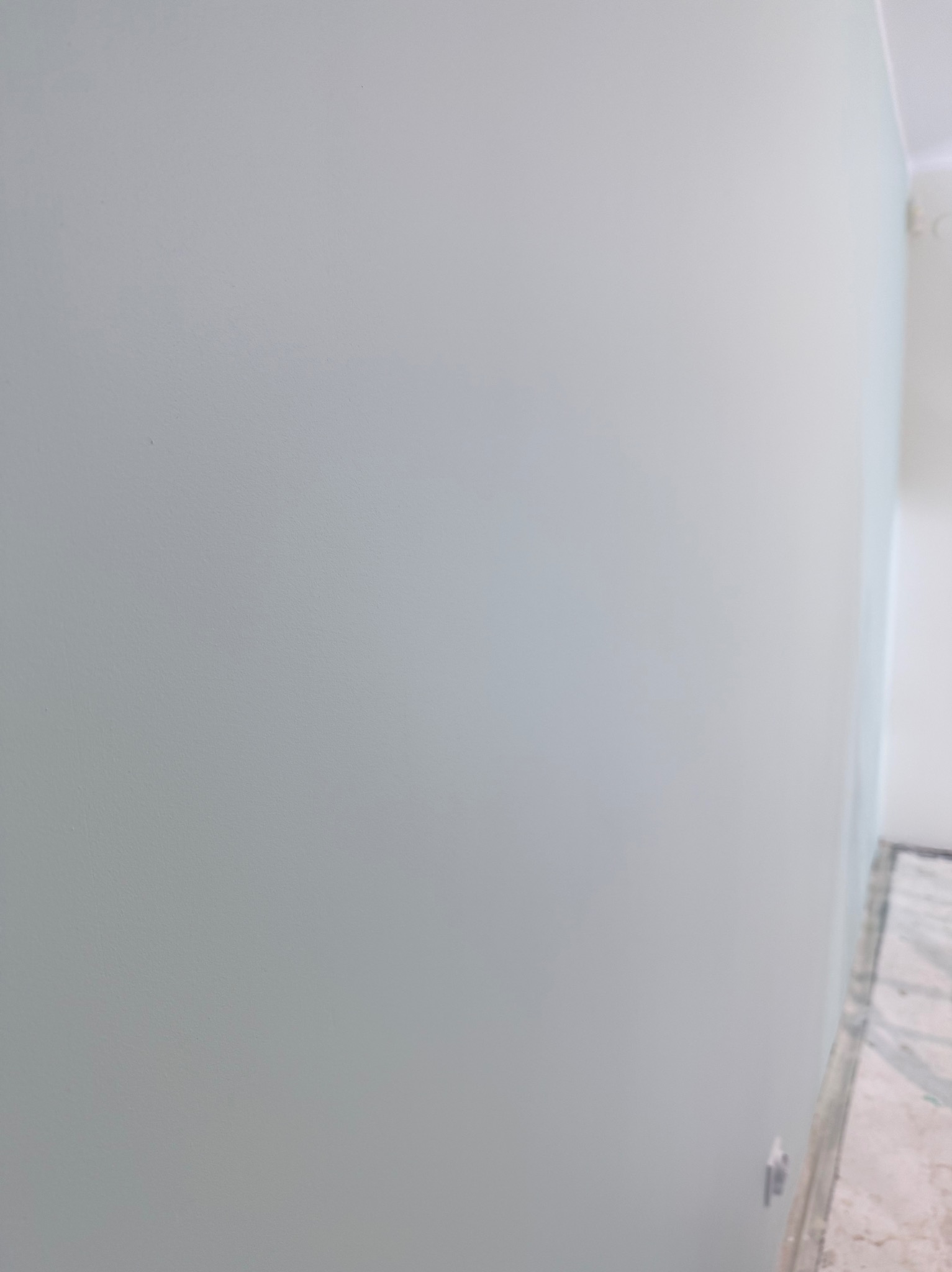 Gładka, świeżo pomalowana ściana w odcieniach szarości, widoczny fragment podłogi z marmurowym wzorem. Minimalistyczne wnętrze po remoncie.