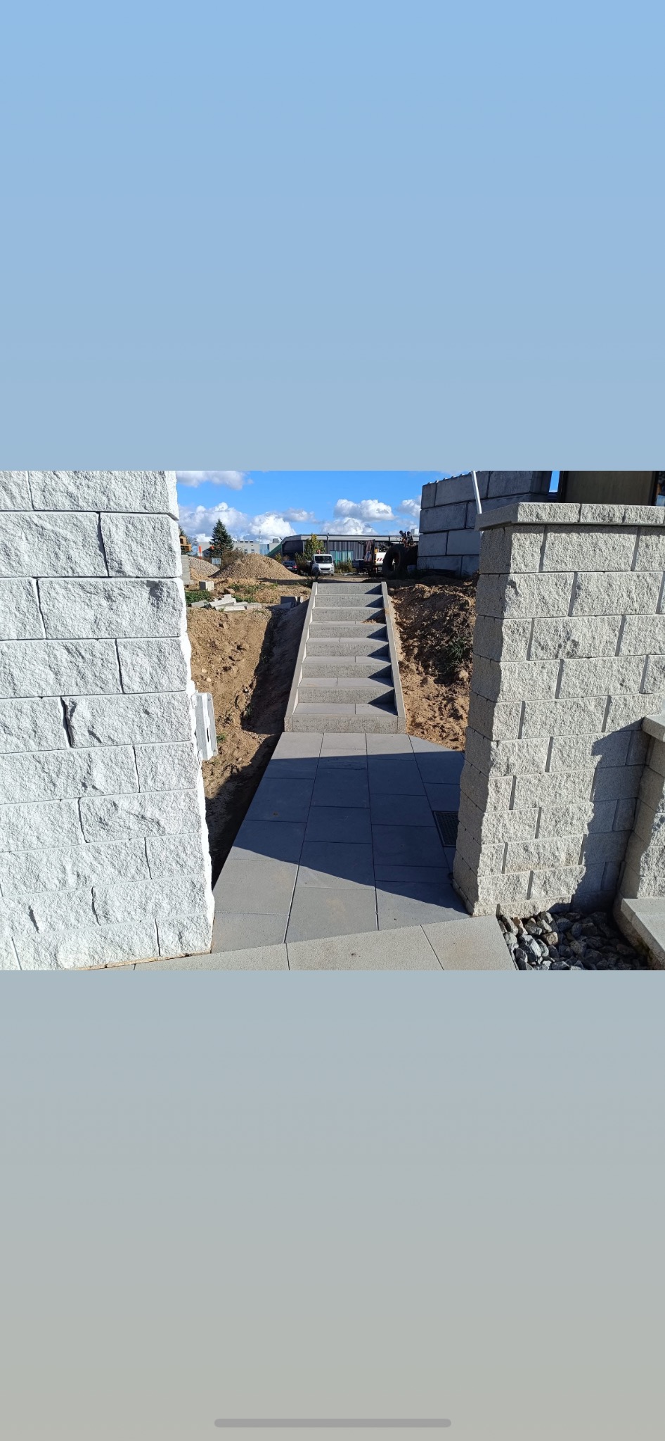 Schody z kostki brukowej prowadzące przez kamienne filary, w tle plac budowy i błękitne niebo. Wykończona ścieżka z kostki brukowej.