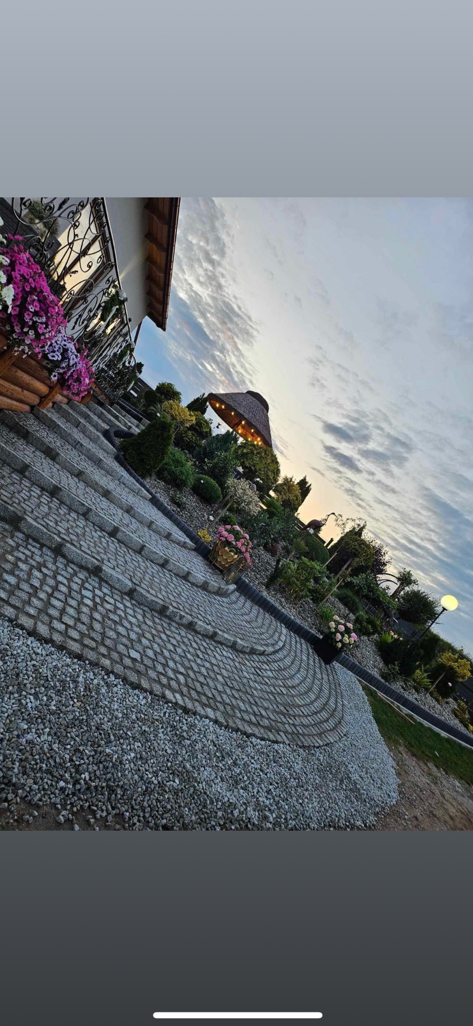 Ukończony taras z kostki granitowej ułożonej w półokręgi, z ozdobnymi roślinami i oświetleniem, widok z boku.