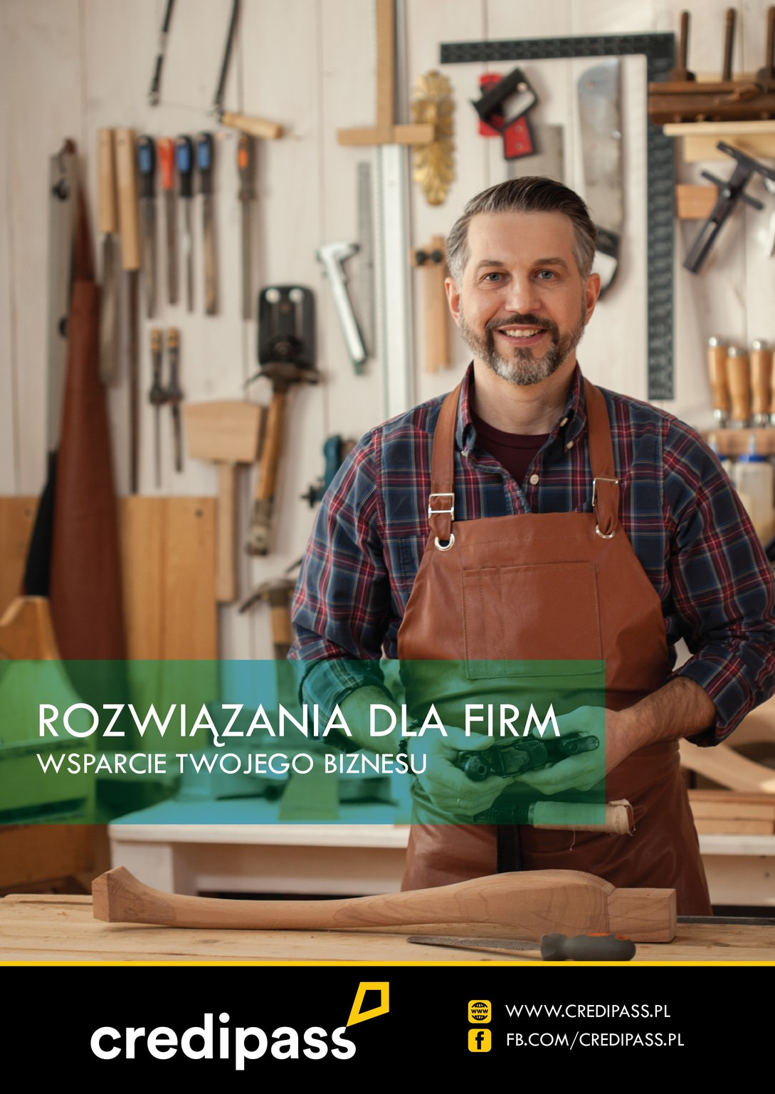 Uśmiechnięty stolarz w skórzanym fartuchu, trzymający narzędzie do obróbki drewna, w tle warsztat z licznymi narzędziami, logo Credipass na dole.